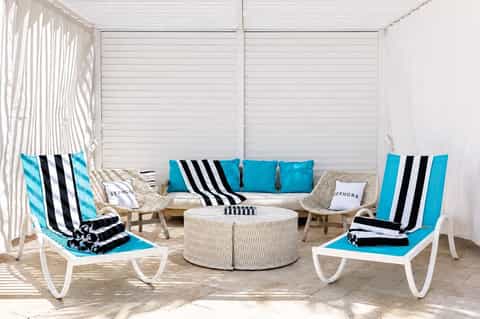 Luxury cabana lounge with striped cushions, turquoise accents, white privacy walls, and woven furniture