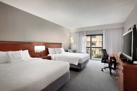 Hotel room with two queen beds, wooden headboard, flat-screen TV, and balcony access with city views