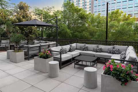 Rooftop lounge with gray sectional sofa, black umbrella, planters with flowers, and city views
