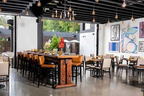 Contemporary dining space with wooden tables, tan leather chairs, pendant lighting, and patio views