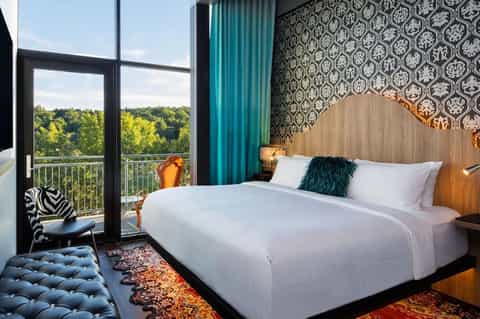 Luxury bedroom with forest-view balcony, king bed, patterned wallpaper, and teal drapes