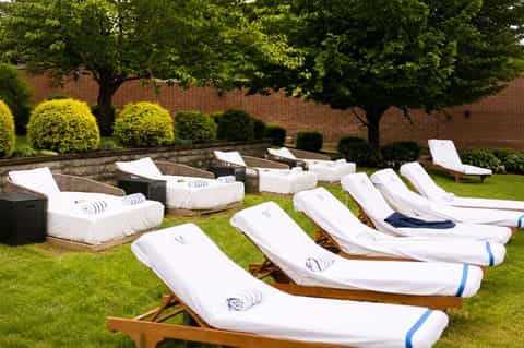Array of white wooden lounge chairs on manicured lawn with topiary and brick walls