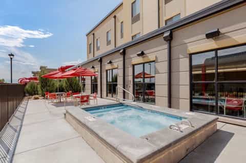 Outdoor hot tub on patio with red umbrellas and lounge chairs beside modern hotel building