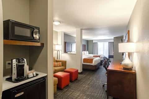 Hotel suite with bedroom, seating area, coffee maker, and warm wood furnishings