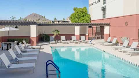 Resort rooftop pool with crystal blue water, white lounge chairs, pink building facade, and mountain views in desert setting