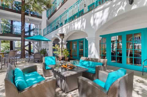 Outdoor courtyard with turquoise lounge seating, fire pit table, tall tree, white arches, and turquoise doors
