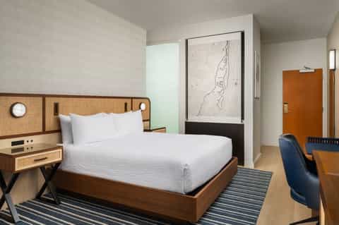 Modern hotel bedroom with woven headboard, white bedding, abstract art, and wood accents