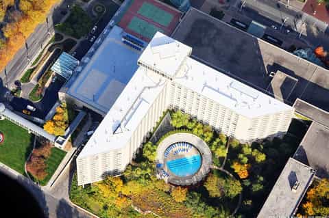 Aerial view of modern hotel with circular pool surrounded by green space and residential buildings