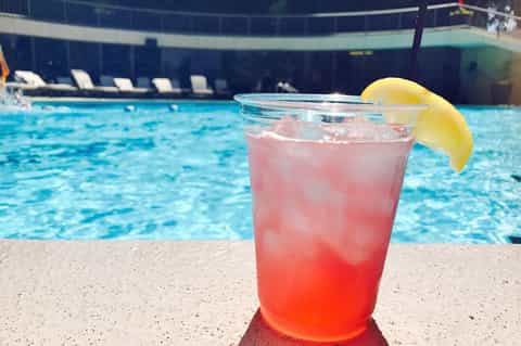 Pink cocktail with lemon slice on pool deck overlooking bright blue swimming pool