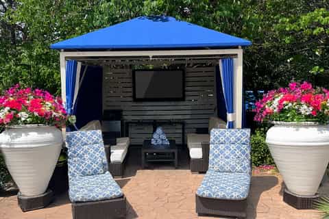 Outdoor gazebo with blue roof, TV, comfortable seating, and colorful flower planters on either side