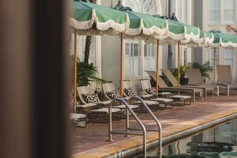 Outdoor poolside lounge area with chaise lounges under green and white striped awning and tropical plants