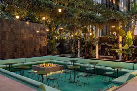 Sunken outdoor lounge area at night with green seating, firepit, lush plants, and warm lighting