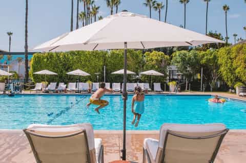 Resort pool with crystal blue water, lounge chairs, large umbrella, and children swimming under palm trees