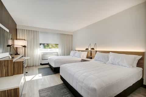 Double queen hotel room with two beds, wooden accents, desk area, and ambient lighting