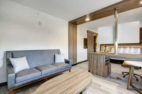 Hotel suite living area with gray sofa, wooden desk, workspace, and modern furnishings