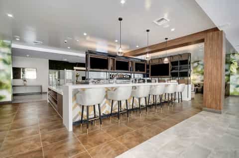 Upscale hotel lounge bar with white seating, wood beam ceiling, pendant lighting, and geometric flooring