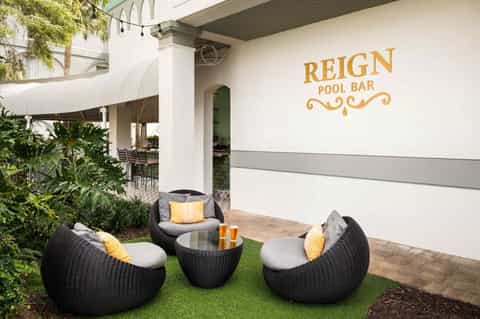 Reign Pool Bar outdoor lounge with black wicker seating, cushions, and tropical landscaping