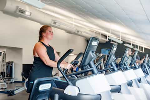 Fitness center with woman on stationary bike surrounded by cardio equipment and bright lighting
