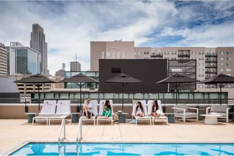 Rooftop pool deck with lounge chairs and umbrellas overlooking Omaha skyline during daytime