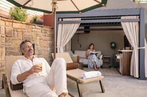 Outdoor cabana space with man relaxing, covered seating area with curtains and stone walls