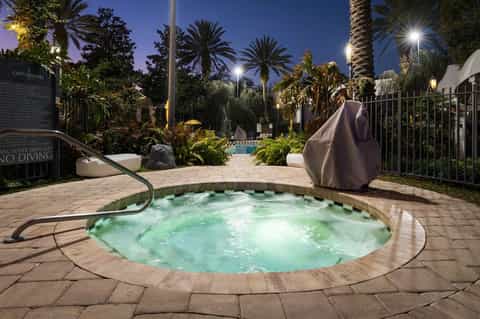 Illuminated spa hot tub at night with palm trees, landscaping, and covered lounge chairs nearby