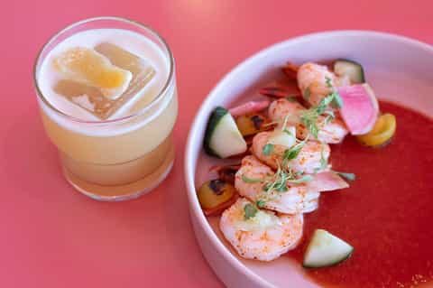 Cocktail with grapefruit garnish and plated shrimp appetizer on pink surface
