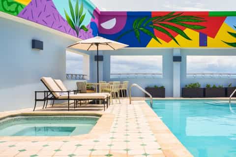 Hotel pool deck with vibrant abstract mural ceiling, lounge seating, hot tub, and ocean views