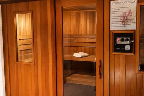 Cedar sauna interior with wooden benches, glass window, control panel, and rolled towels