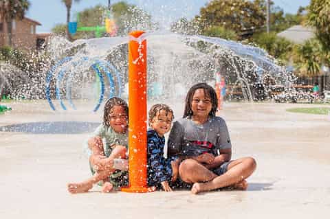 Children playing in interactive water splash pad with orange center column and spraying water