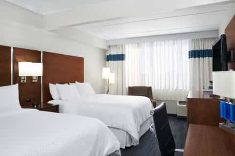 Hotel guest room with two queen beds, brown headboards, and city windows