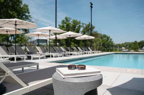 Modern resort pool deck with white umbrellas, gray loungers, and manicured landscaping under blue sky