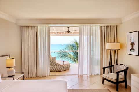 Luxury beachfront hotel room with ocean view terrace, elegant furnishings, and direct access to white sand beach