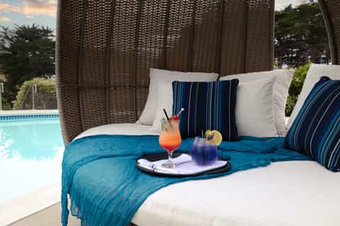 Wicker pod lounge chair by pool with blue cushions, cocktails, and ocean view