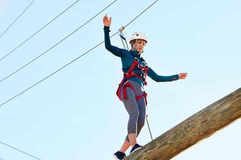 Woman zip-lining on wooden beam wearing safety helmet and harness with cables overhead