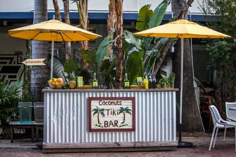 Coconuts Tiki Bar with yellow umbrellas, tropical plants, and palm trees