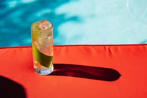 Cocktail with lime and ice on red pool lounger overlooking turquoise water