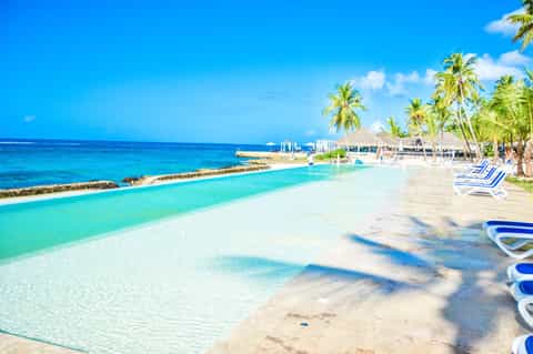 Crystal clear lagoon pool with white sand beach, palm trees, and lounge chairs