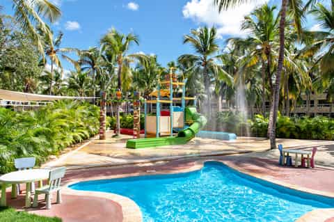 Resort pool with colorful playground, water slide, and palm trees in tropical setting