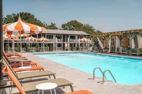 Resort pool with orange and white striped umbrellas, orange lounge chairs, pergola seating, and tan loungers