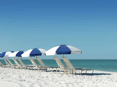 Row of blue and white beach umbrellas with lounge chairs on white sand facing calm turquoise water
