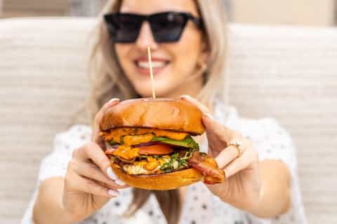 Woman holding a gourmet burger with multiple layers and fresh toppings