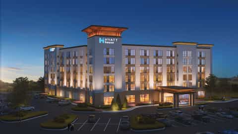 Hyatt House hotel exterior at dusk with illuminated facade, parking lot, and landscaping under clear blue sky