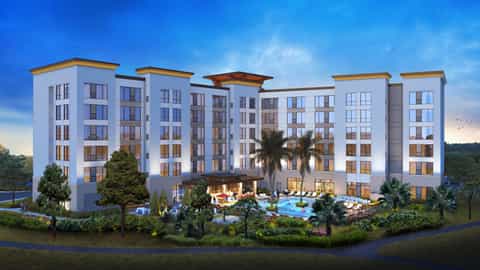 Resort exterior with white multi-story building, pool area, palm trees, and waterfront setting at twilight