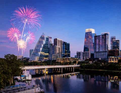 Austin skyline at dusk with fireworks exploding over downtown buildings reflected in the Colorado River