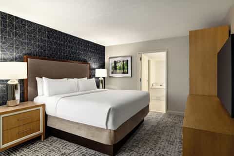 Hotel bedroom with queen bed, wood nightstands, geometric accent wall, and ensuite bathroom entrance