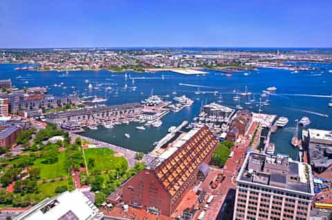Aerial view of scenic waterfront city harbor with sailboats, green parks, and dense urban architecture