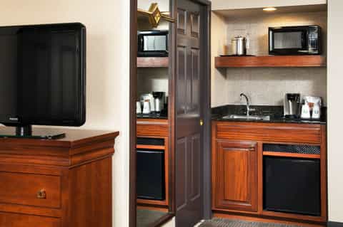 Hotel suite kitchenette with wood cabinetry, black appliances, and dark countertops