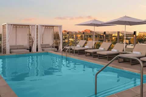 Resort pool with cabanas, loungers, umbrellas, and desert mountain landscape at sunset