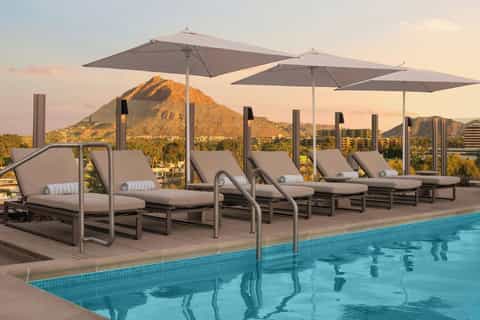 Rooftop pool with lounge chairs and umbrellas overlooking a desert mountain at sunset