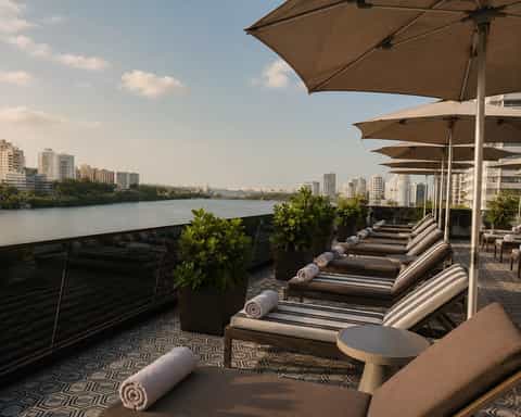 Waterfront lounge deck with chaise lounges under umbrellas overlooking a river and city skyline